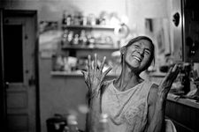 Aiyyana Maracle smiles and throws up her hands in possibly an expression of joy. The portrait is monochrome and the background, while blurry, suggests an interrior space such as a kitchen or studio. Aiyyana is Indigenous, has her hair pulled back and wears a sleeveless top with a subtle floral design.
