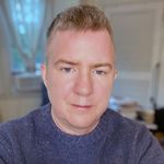 Chet Pancake has a sombre expression, blue eyes, light-skin, and short hair. The wear a pullover. The blurred background suggests they're in a home office.