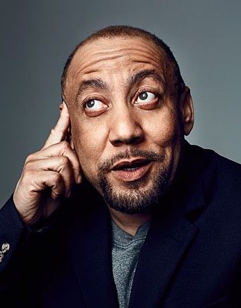 Kylar W. Broadus looks like they are talking animatedly while his finger rests on his temple. Kylar is a light-skinned Black person with a buzzcut and short goatee. He wears a t-shirt and blazer.