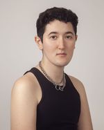 Morgan Sullivan is trans with very light skin in front of a white gray background. They are wearing a black muscle t-shirt with two silver chains shown from the abdomen up. They have short black hair with faded sides.