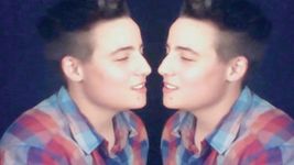 Using a mirror symmetry tool, this still creates the illusion that a person is connecting and flirting with themself. The person wears a blue, red and purple flannel and has short brown hair with high faded sides. The background is a deep blue colour.