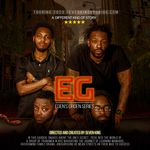 Four people with dark brown skin are posed in front of a city landscape. Two people are sitting on the couch in front of two other people who are standing behind the people on the couch. The person sitting on the left has short black hair with waves, dark brown skin and a black shirt. The person sitting on the right has dark brown skin and has long dreadlocks and is wearing glasses. The person standing on the left is crossing their arms and wearing a black t-shirt. They have a tattoo on their forearm and a beard with short curly hair. The person standing on the right is leaning forward and placing their hands on the couch. They have tattoos covering their arms, and they have a beard and short dreadlocks. All four stare into camera with serious expressions.