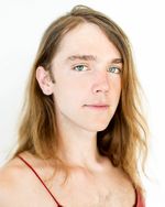A soft and polished portrait of Zachary Clarence looking directly into the camera with a calm expression and standing in front of a glowing white backdrop. They have light skin and long, blond hair, and are wearing a thin-strapped tank top.