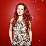Gretchen Wylder standing against a grungy red wall. Gretchen has light fair skin, brown eyes, and long, fire-red hair. She is wearing a sleeveless animal print dress.