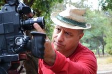 Brian Favorite adjusts the focus on a camera lens. He has a look of concentration, light skin and short hair which peeks out from under a straw fedora.